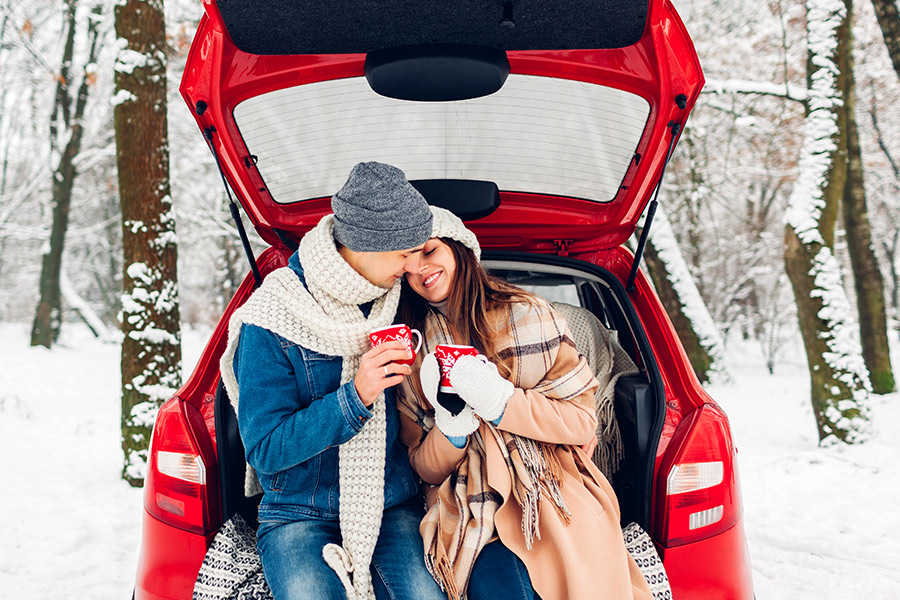 Couple Sitting in Back of Car & Drinking from Mugs During Winter