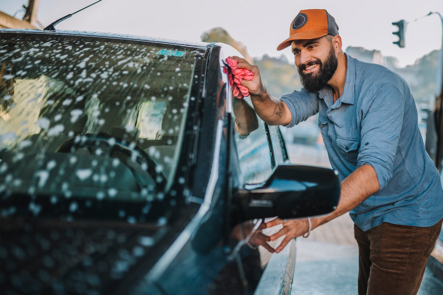 Happy Bearded Man in a Hat Washing His New Car