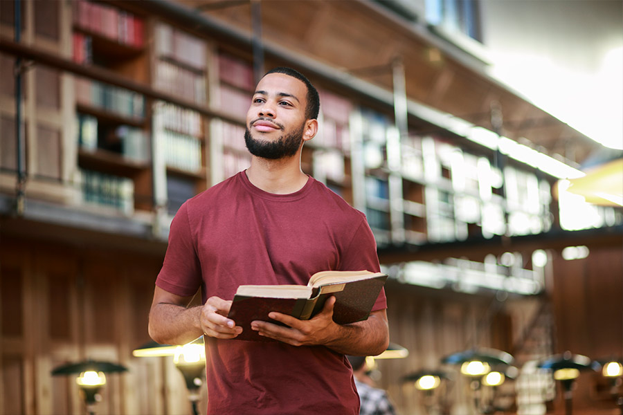 Man Holding a Book in a Library Studying Financial Literature