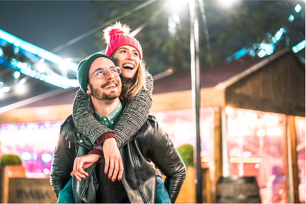 A man smiles at a woman riding on his back while walking outside