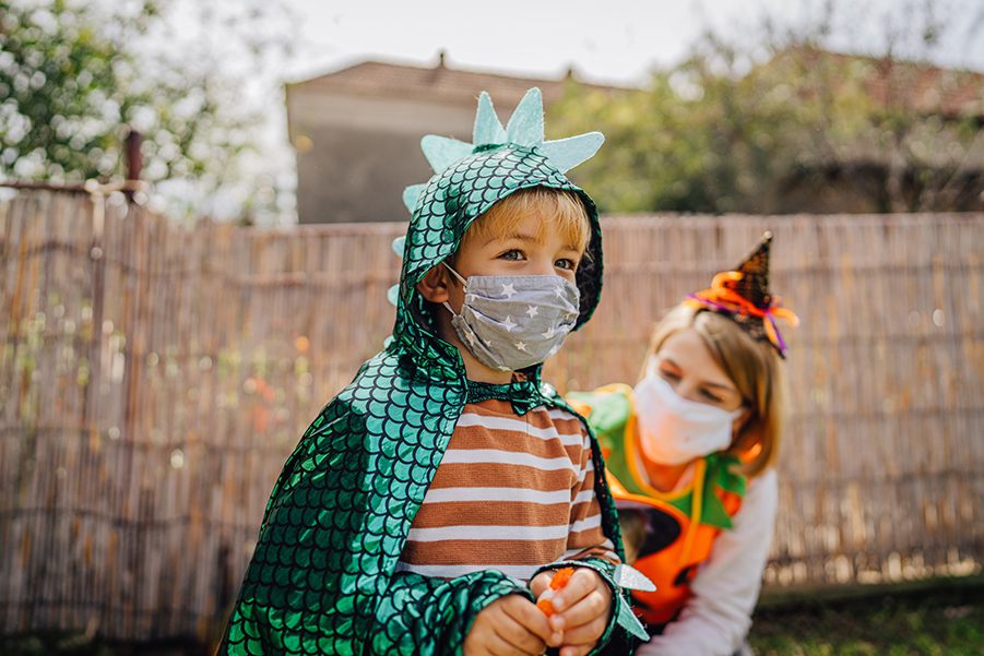 Boy in dragon costume wearing a protective face mask on Halloween.